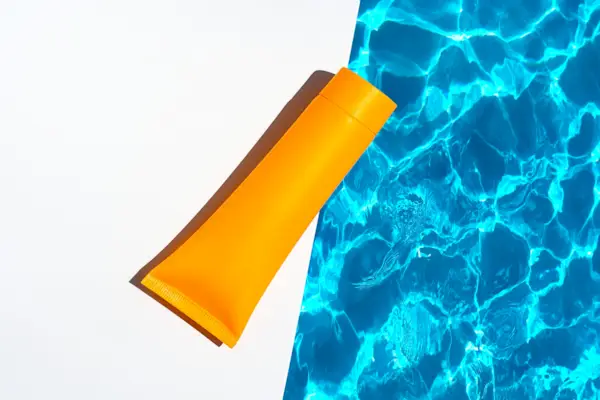 Orange tube with suntan lotion, cosmetic face cream or hand cream, shower gel, shampoo against the background of blue turquoise water with waves from the swimming pool.