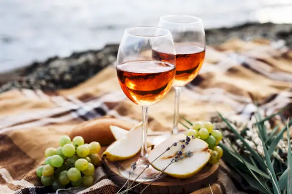 Two glasses of wine and summer fruits on the beach, sea and landscape in background, summer picnic, idea for outdoor weekend activity