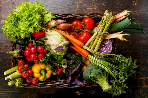 Fresh vegetables in basket on wooden background