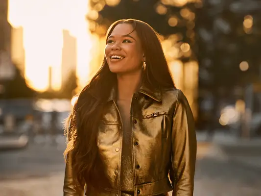 Storm Reid outdoors, wearing a shiny jacket and smiling