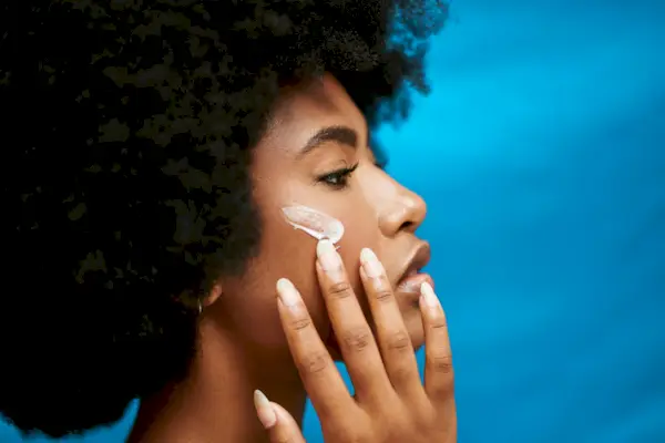 A young African model applying lotion to her skin. A closeup of a beautiful nude woman with a dark complexion using a cream for face care in studio against a blue background