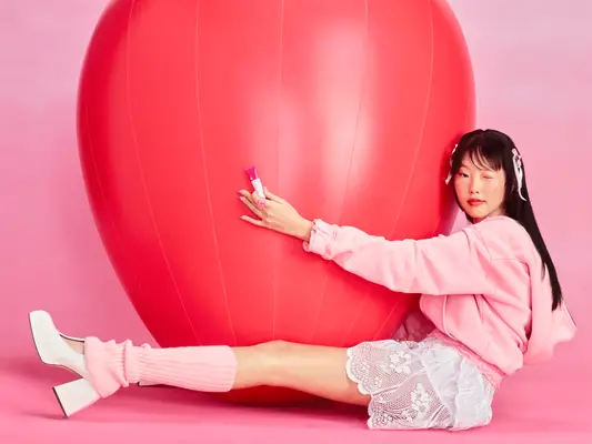 Model applying the Glossier Strawberry Balm Dot Com