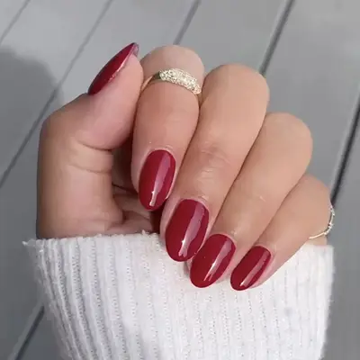 Close up of a cranberry-colored manicure, hand folded and holding the cuff of a white sweater