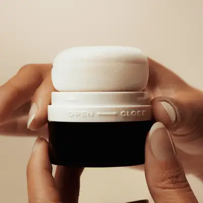 A hand holding an open Ceremonia pouf