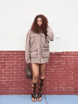 Angel Reese standing in tan dress in front of brick wall