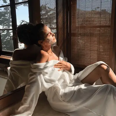 Cindy Crawford wearing a white robe and a face mask in her bathroom