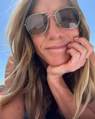 Jennifer Aniston smiles ina. selfie showing off her sheer pink nail polish.