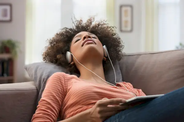 Black woman listening to headphones on sofa