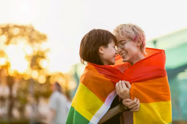 Young non binary couple in love hugging under a rainbow flag