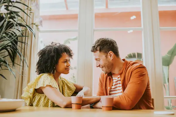 A beautiful young couple looks very much in love as they sit at a dining table sipping hot drinks and flirt.