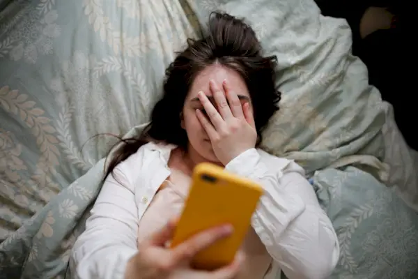 Young woman with flowing hair using phone on bed, close face palm. Top view