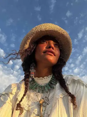 model wearing white blouse, layered necklaces, raffia bucket hat
