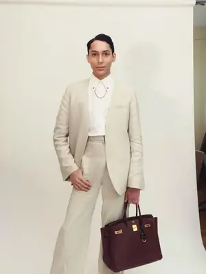 Charles Gross wearing a neutral suit and carrying a dark brown Hermes Birkin bag