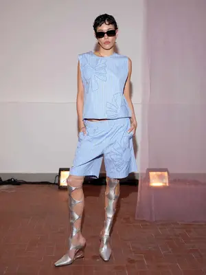 Person poses in blue short and blouse set with sculptural silver Gladiator heels