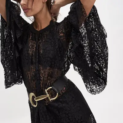 Lori Harvey wears a sheer white top, neutral bikini top, white shorts, brown handbag, and sunglasses