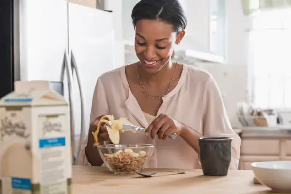 Mixed race woman eating cereal and banana in kitchen
