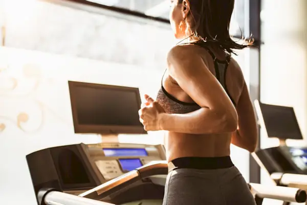 Sweaty female athlete running on treadmill during sports training in a health club.