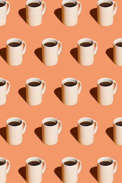 Mugs of black coffee in rows against peach background