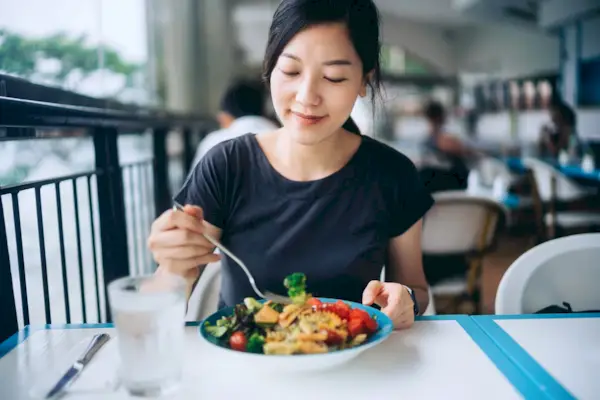 Young Asian woman enjoying a healthy meal for lunch. She is having fresh and colourful vegan salad bowl with organic greens and fruits at a vegan restaurant. Healthy eating, go green lifestyle