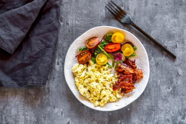 Scrambled eggs with fried bacon and salad with tomato, low carb, from above