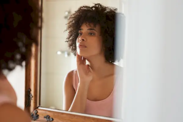 Young African woman examining her skin in a bathroom mirror