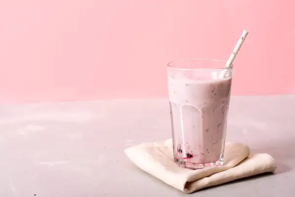 Two glasses of blueberries smoothie on pink background. Poring from blender into glass.