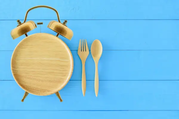 Intermittent fasting, diet and weight loss concept : Clock shaped wood dish, spoon and fork. Eco-friendly plate / kitchen utensil as alarm clock with ringing bell, depict alert or reminder time to eat