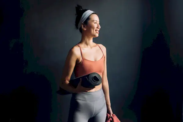 Ready for Yoga: Waist Up Portrait of a Happy Asian Woman in Sports Clothes Holding an Exercise Mat