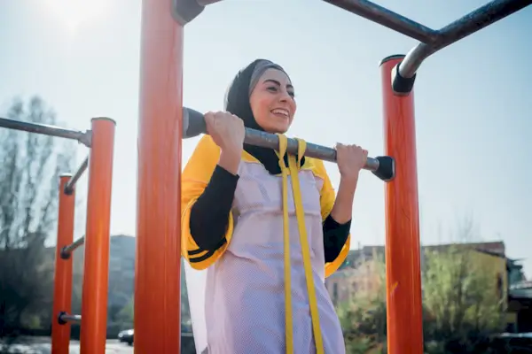 Calisthenics at outdoor gym, young woman doing pull up on exercise equipment