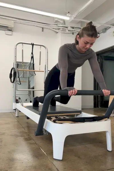 Fitnessredakteurin Talene führt eine Pilates-Sequenz mit ihren Händen auf der Fußstange des Allegro 2 Pilates Reformer-Geräts durch