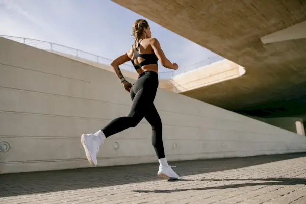 Back view of woman athlete in sportswear is running on buildings background. Active life concept