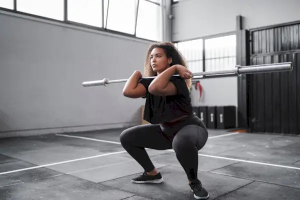 Curly haired young woman practicing squats in gym