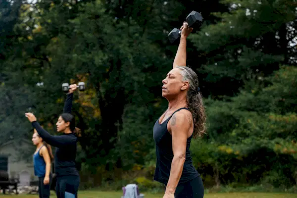 Mature woman working out with dumbbells during outdoor fitness class