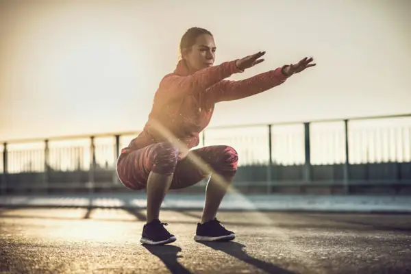 Young woman doing squats on a road at sunset.