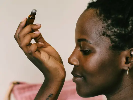 Closeup profile of a young black woman smelling essential oil she applied on her wrist.