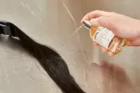 A person sprays Le Labo Santal 33 Eau de Parfum onto hair