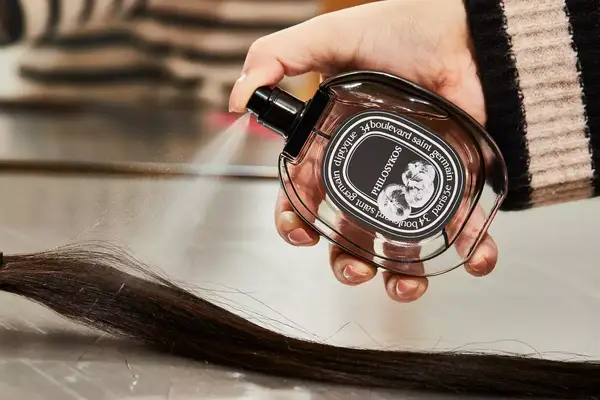 A person sprays Diptyque Philosykos onto hair