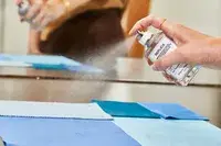 A person sprays Maison Margiela Replica Lazy Sunday Morning Perfume onto fabric