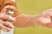 A person sprays Maison Margiela Replica Lazy Sunday Morning Perfume onto their wrist