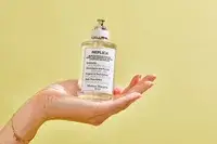 A person holds up a bottle of Maison Margiela Replica Lazy Sunday Morning Perfume