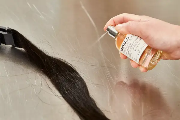A person sprays Le Labo Santal 33 Eau de Parfum onto hair