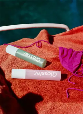 Glossier body spritzes laying on a towel.