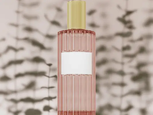 A pink ridged bottle of fragrance with a blank white label, gold cap, and the shadows of leaves behind it