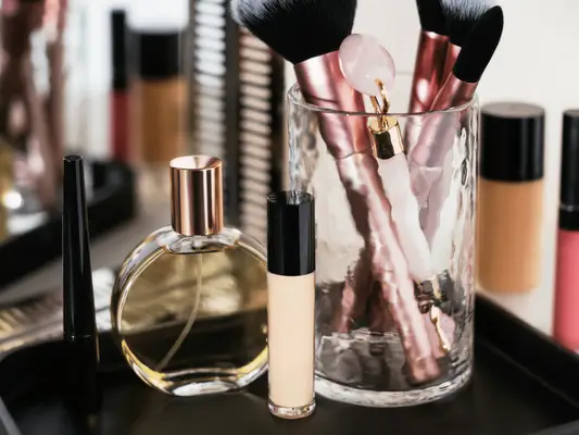 The top of a vanity with a bottle of perfume, a perfume rollerball, makeup brushes and other beauty items
