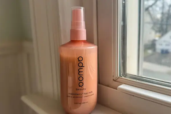 A bottle of Adwoa Beauty Hair Milk Leave-In Conditioner with Melonberry on a windowsill