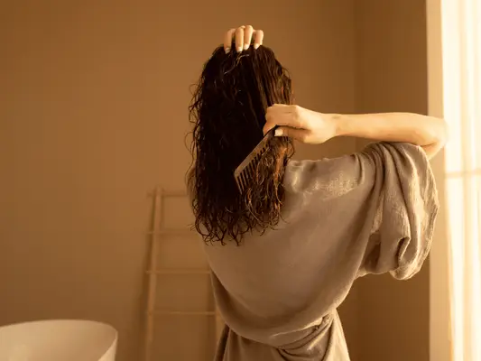 The back of a woman in a bathrobe combing out her wet hair