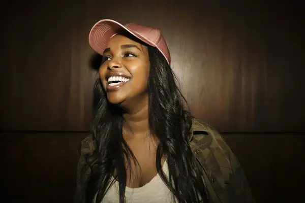 Young black woman with curly hair and a pink satin baseball hat on