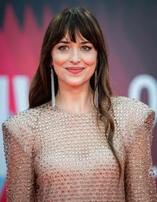Dakota Johnson at a film premiere in a studded dress with shoulder pads and long, wispy bangs