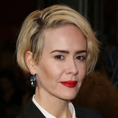 Sarah Paulson wears a bleach blonde side swept grown out pixie with a bold brow and red lip in NYC
