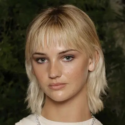 Mia Regan wears a shaggy layered cut with wispy french bangs on her thin blonde hair